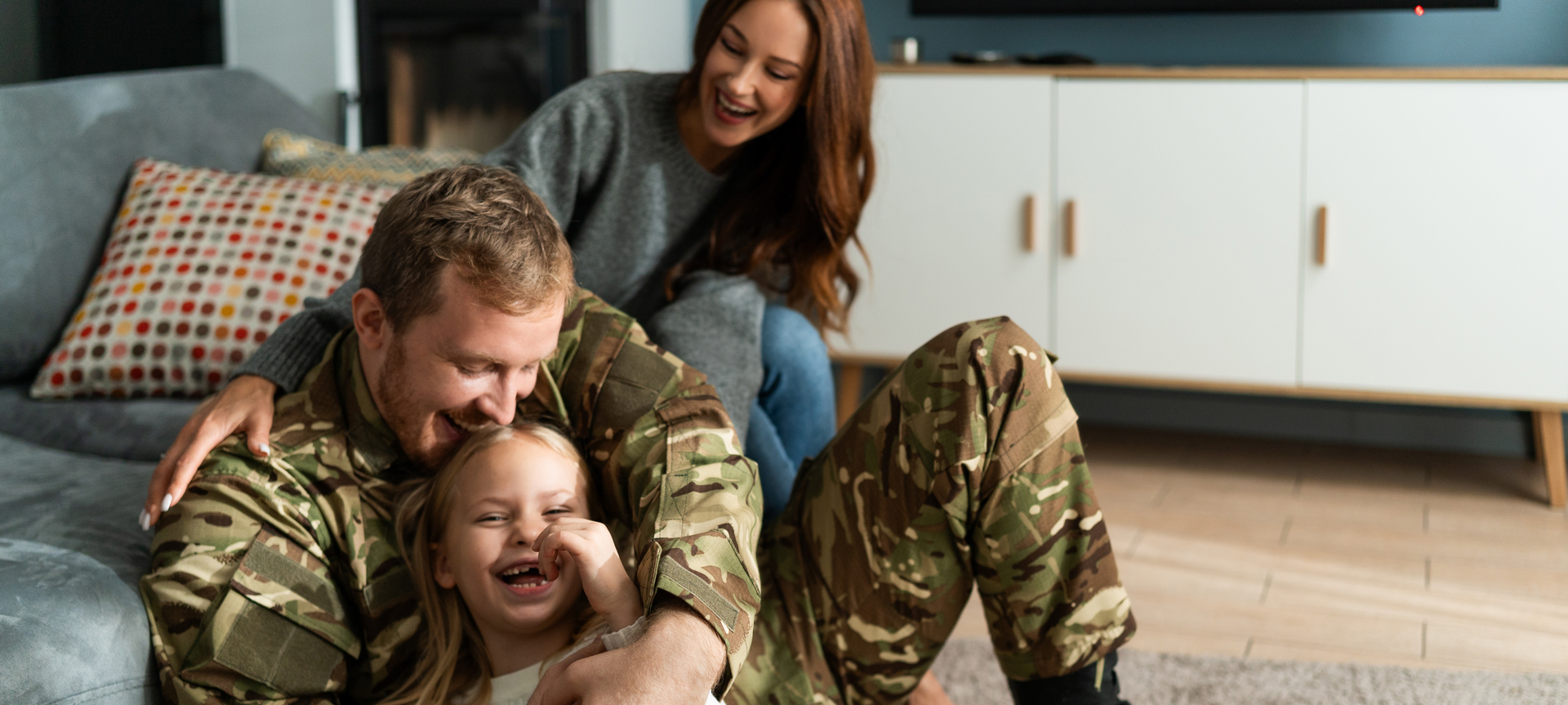 Overjoyed soldier tickling small daughter while sitting at home on the floor