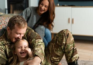 Overjoyed soldier tickling small daughter while sitting at home on the floor