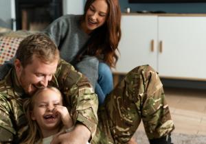 Overjoyed soldier tickling small daughter while sitting at home at the floor