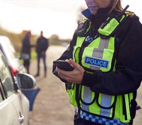 Image showing a police officer holding a mobile phone next to a car